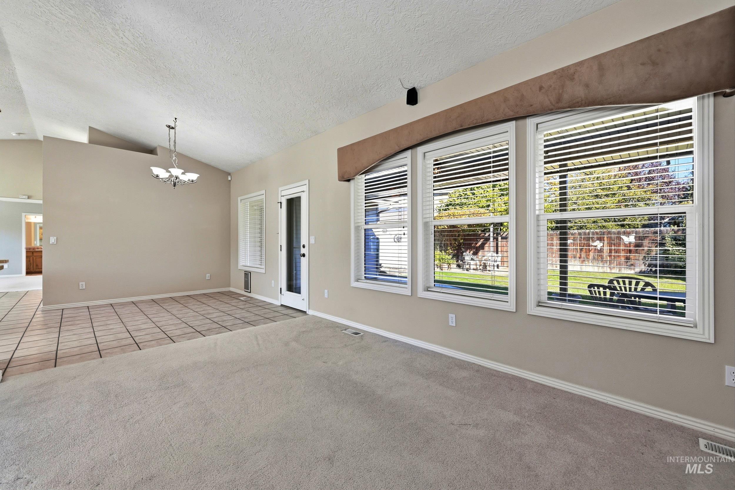 Carpeted spare room featuring tile patterned flooring, vaulted ceiling, a textured ceiling, plenty of natural light, and a chandelier