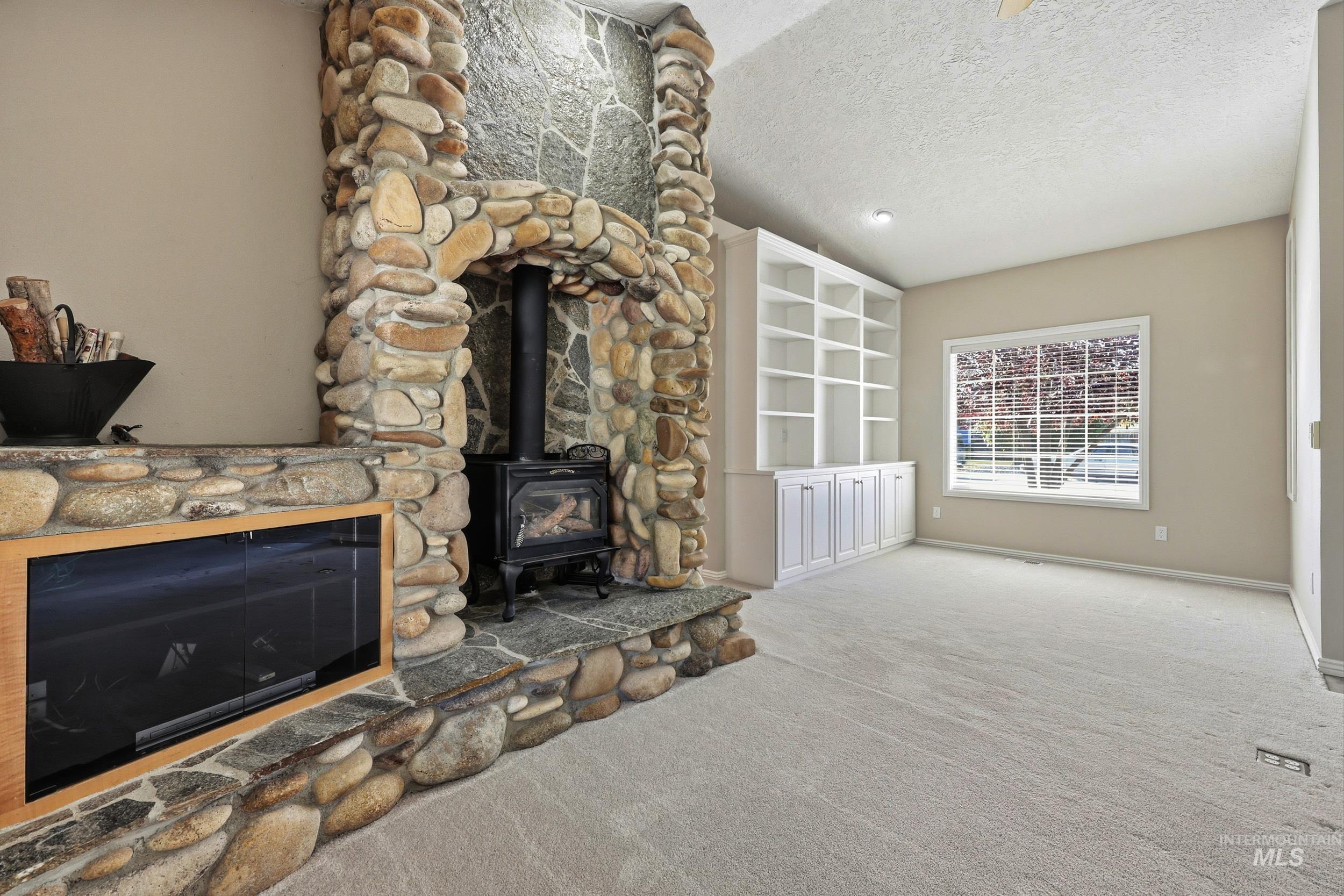 Unfurnished living room featuring carpet flooring, a wood stove, and a textured ceiling