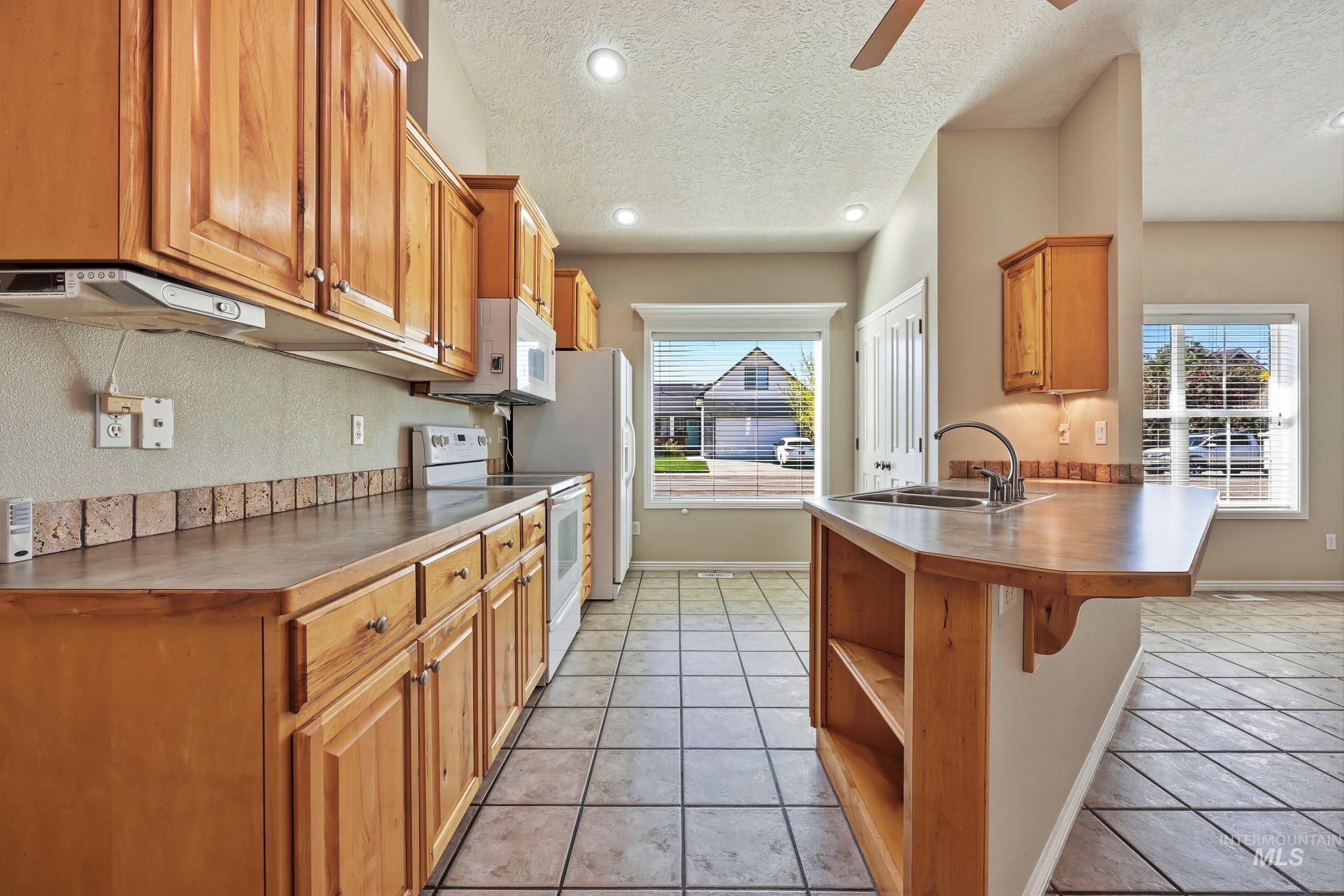 Kitchen featuring a peninsula, white appliances, a breakfast bar, light tile patterned flooring, and a textured ceiling