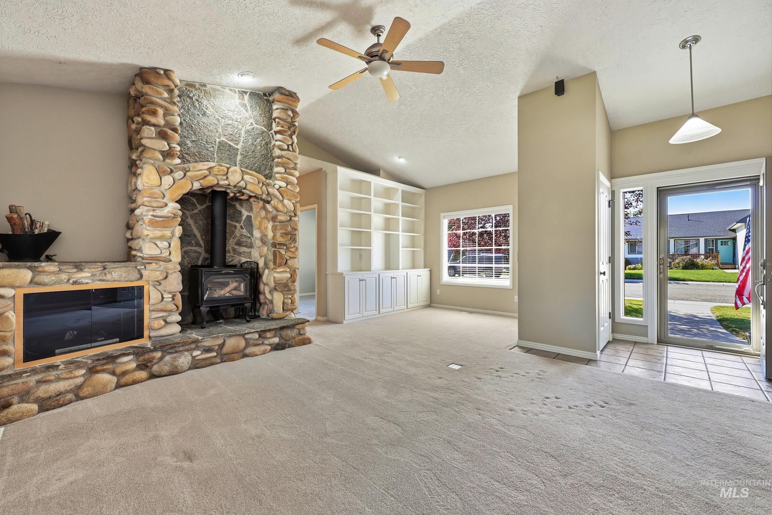 Unfurnished living room with a textured ceiling, a wood stove, lofted ceiling, a ceiling fan, and carpet
