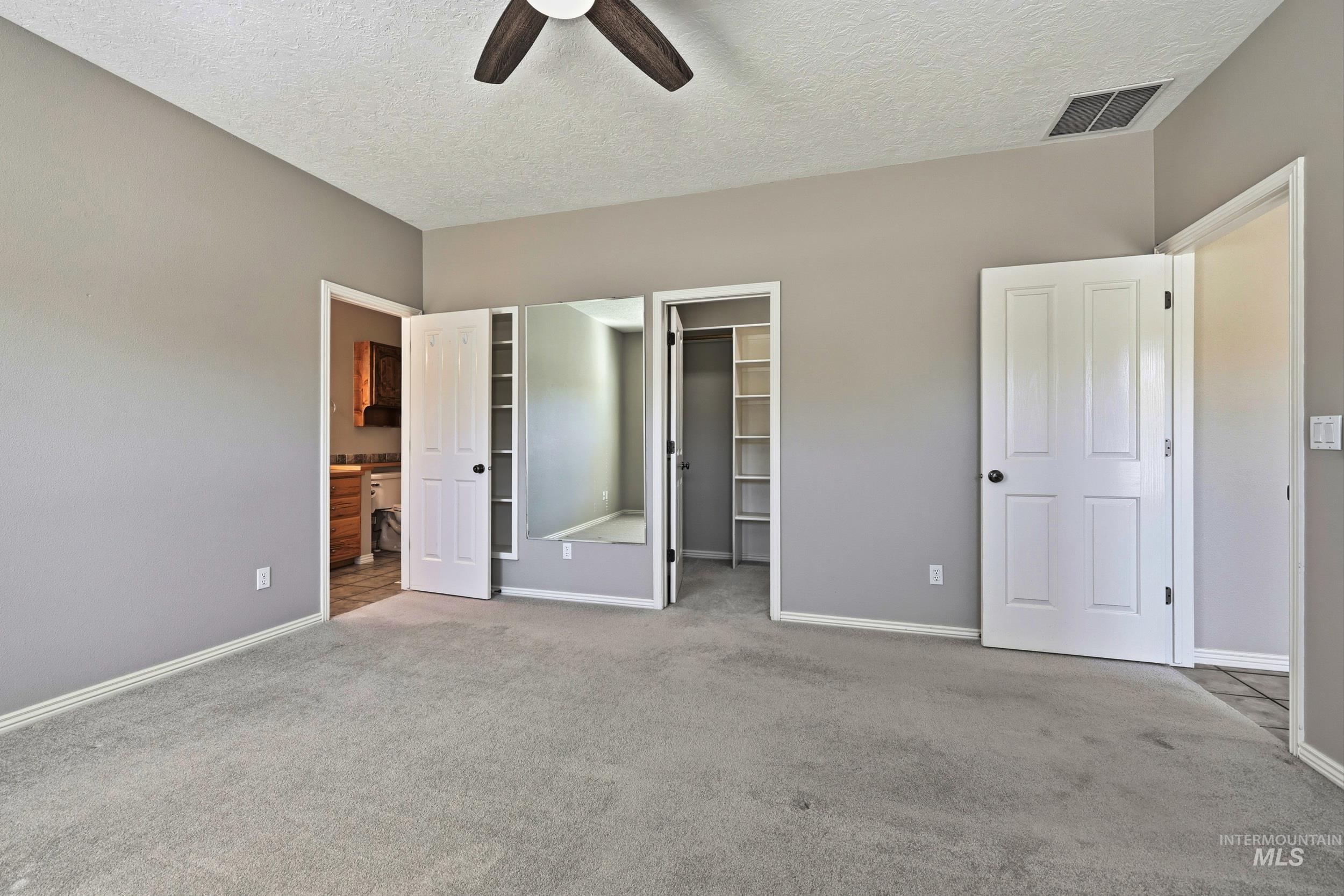 Unfurnished bedroom with a spacious closet, carpet flooring, a textured ceiling, a ceiling fan, and connected bathroom