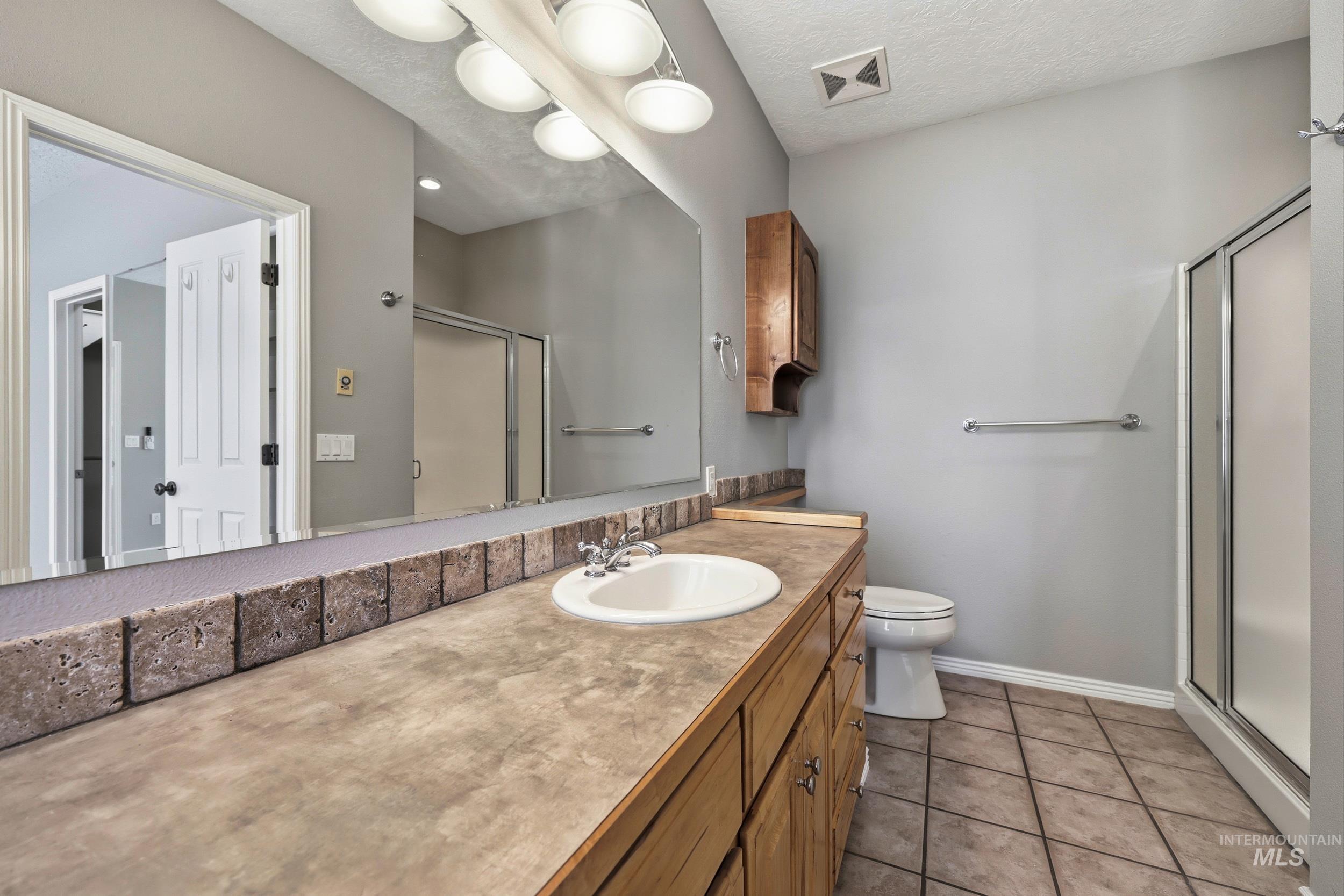 Bathroom featuring a shower stall, light tile patterned floors, vanity, and a textured ceiling