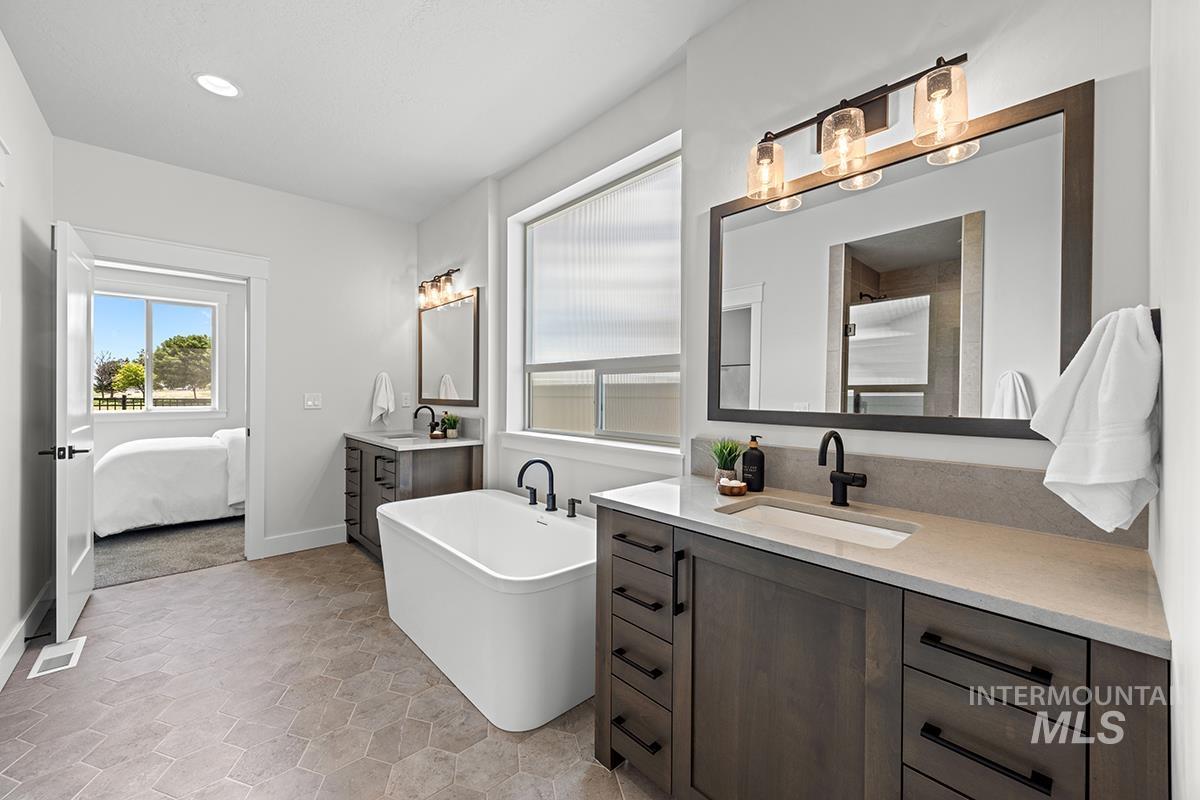 Spacious bathroom featuring a freestanding tub, hexagonal floor tiling, and a dual vanity with dark wood-finish cabinetry and light countertops