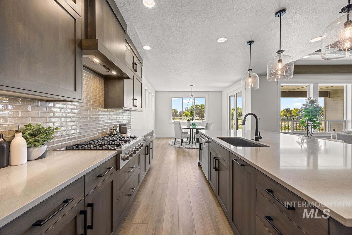 Gourmet kitchen featuring a gas range, subway tile backsplash, contemporary pendant lighting, light wood-finish flooring, and a spacious island with an undermount sink