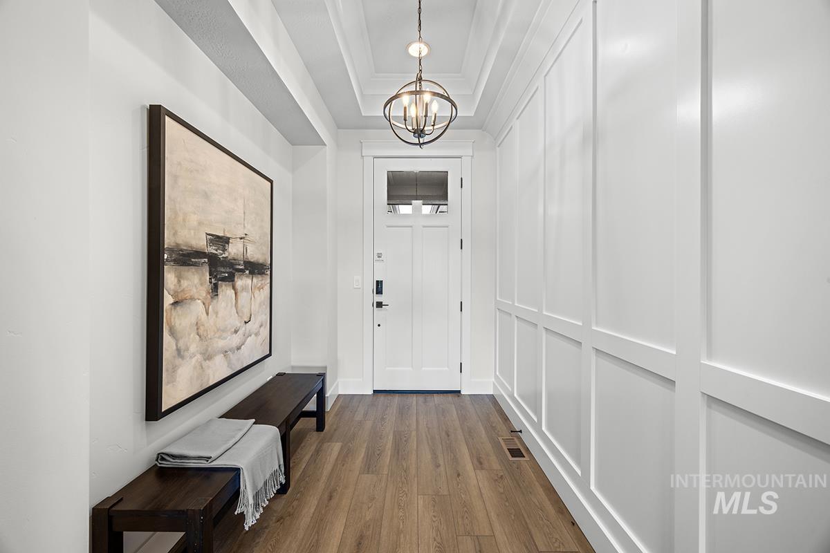 Entryway featuring wood-finish flooring, white paneled accent wall, a coffered ceiling, and a contemporary orb pendant light
