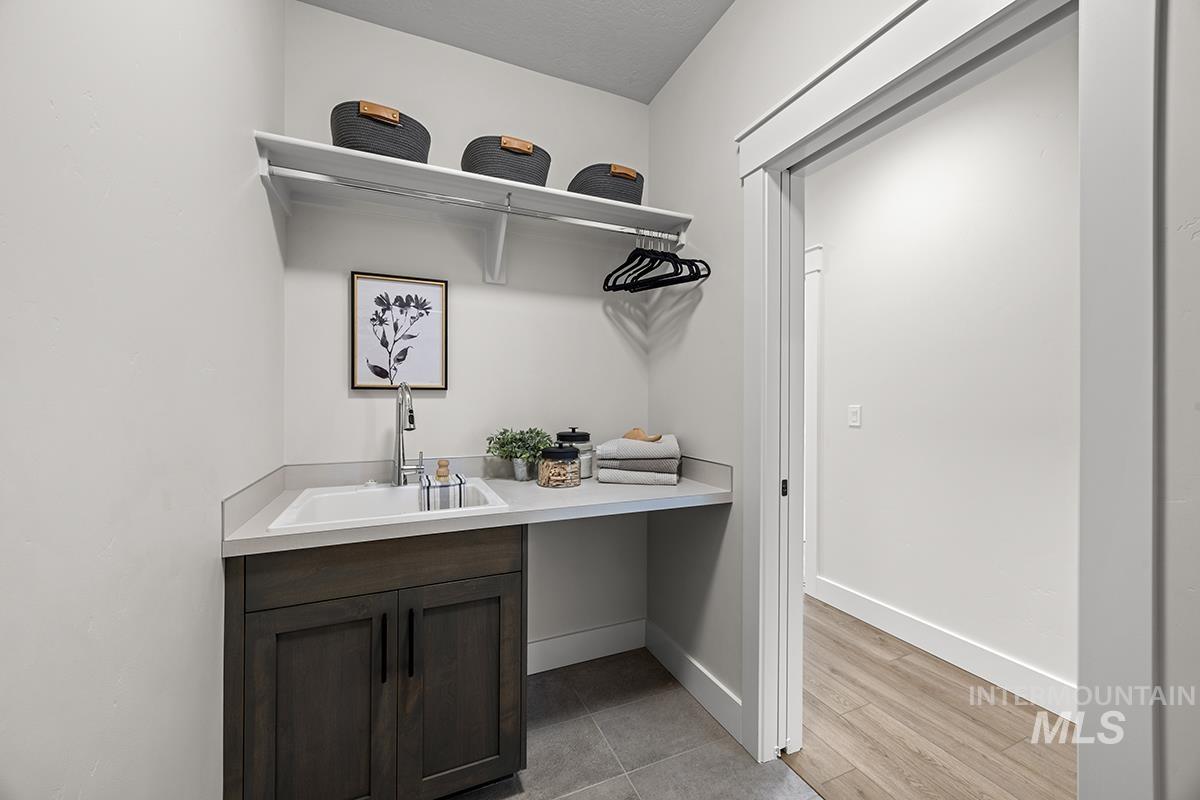 Dedicated laundry area featuring a utility sink with a stainless steel faucet, dark wood-finish cabinetry, and a light-toned countertop