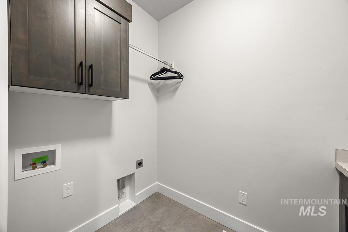 Dedicated laundry space featuring dark wood-finish cabinetry, a built-in hanging rod, a utility sink with a light-toned countertop, and tile flooring