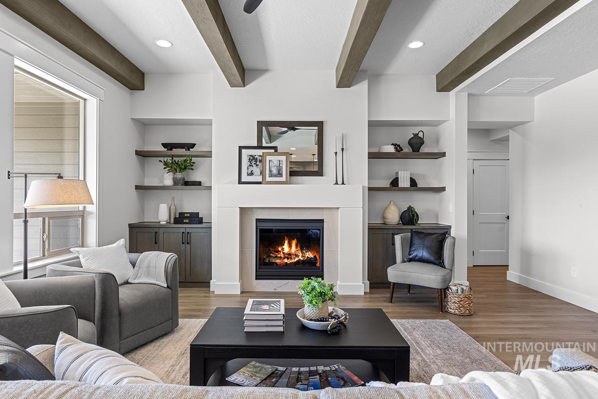 Living area featuring a central fireplace with a substantial mantel, built-in shelving, integrated cabinetry, wood-finish flooring, and exposed ceiling beams