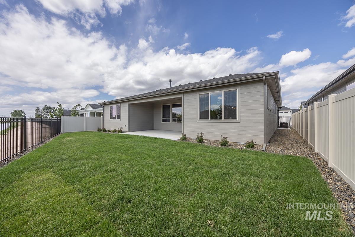 Expansive rear yard with a covered patio, a manicured lawn, and a black wrought iron fence