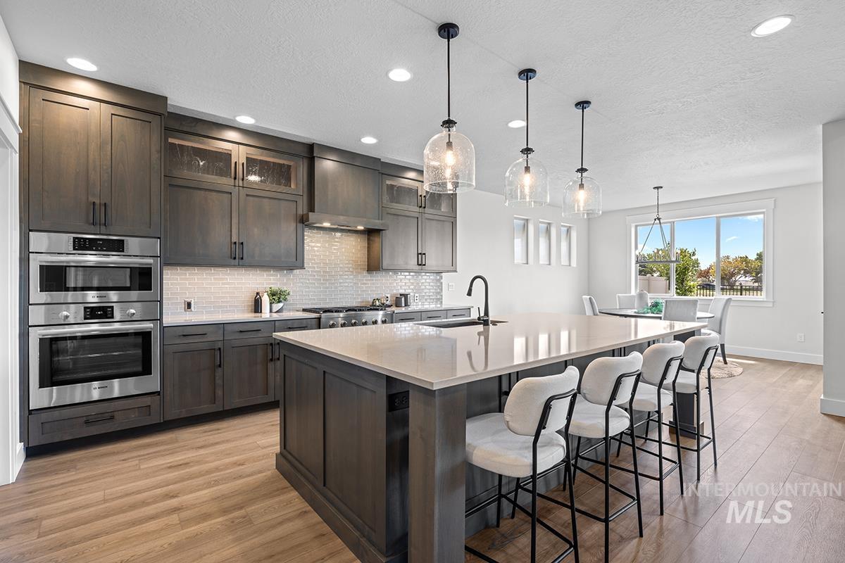 Contemporary kitchen featuring dark wood-finish cabinetry, stainless steel double wall ovens, a tile backsplash, and a large island with integrated seating