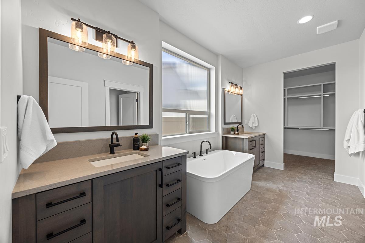 Contemporary bathroom featuring a freestanding soaking tub, dual vanities with quartz countertops, dark wood-finish cabinetry, and hexagonal tile flooring