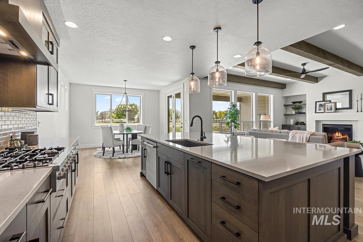 Open-concept kitchen featuring a spacious island with a countertop sink, three pendant lights, and integrated dishwasher