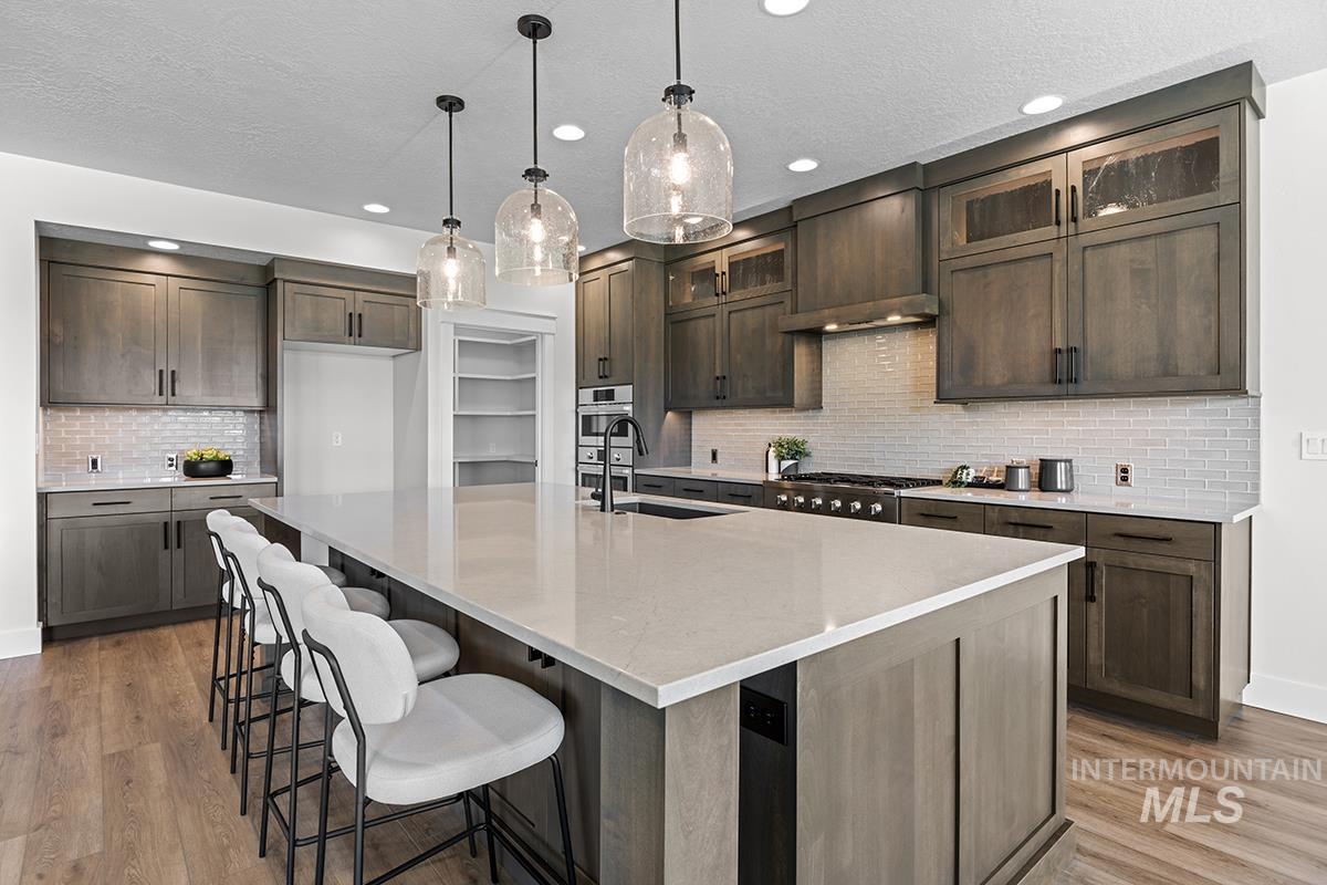 Kitchen featuring a large central island with seating, wood-finish flooring, dark wood cabinetry, light subway tile backsplash, and recessed lighting