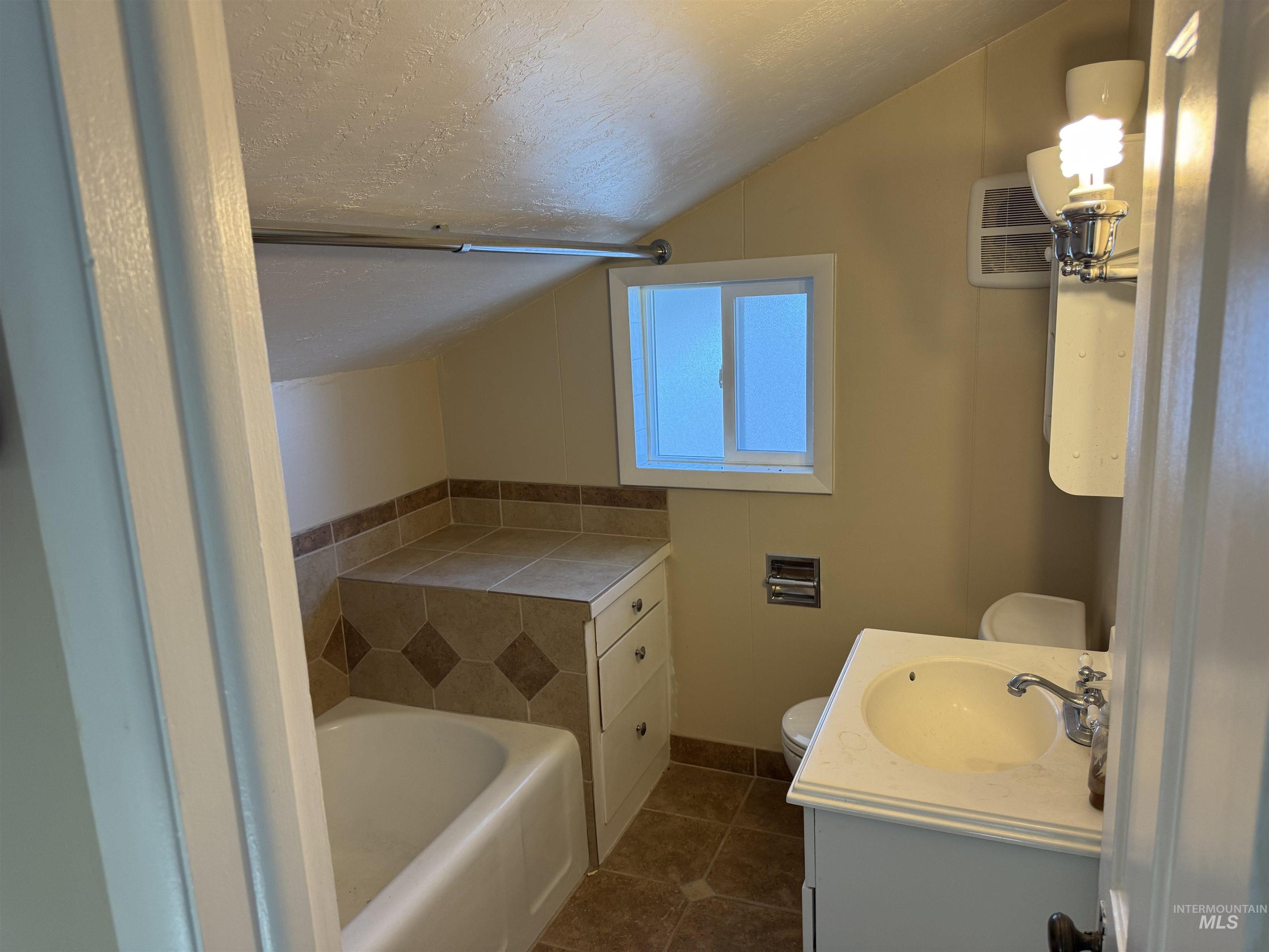Full bath featuring a textured ceiling, dark tile patterned floors, vanity, and lofted ceiling