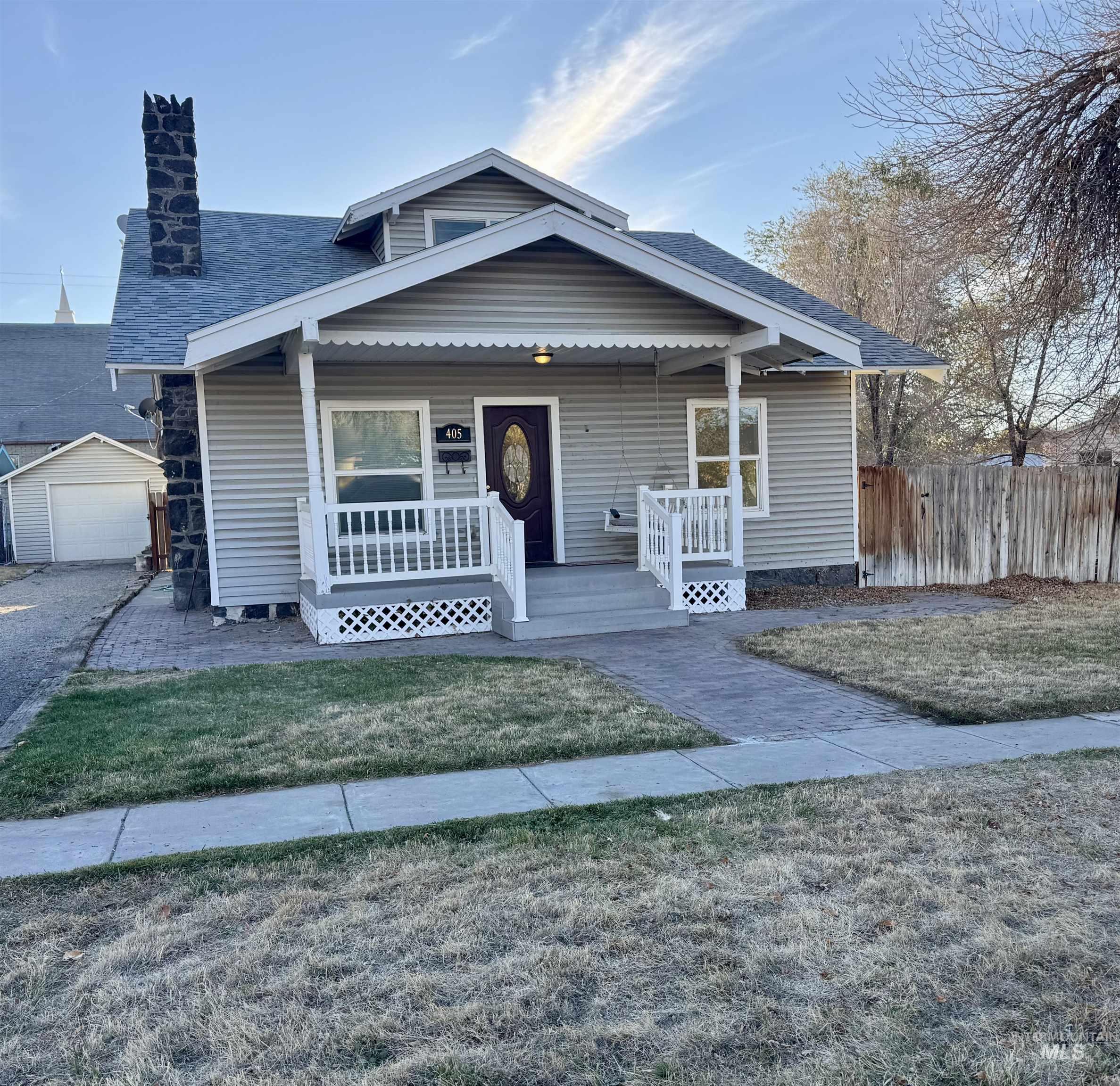 Bungalow-style home featuring covered porch, a chimney, and a detached garage