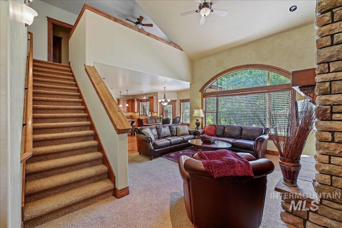 Living area with carpet, stairway, a ceiling fan, high vaulted ceiling, and a chandelier