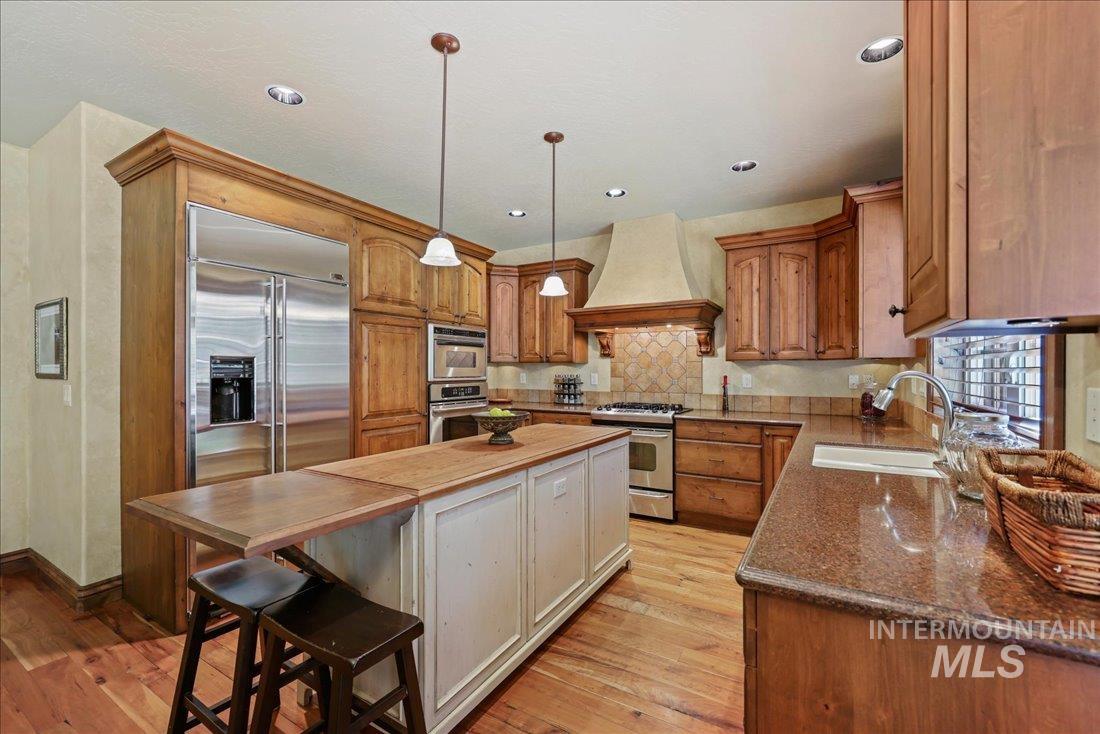 Kitchen with stainless steel appliances, custom exhaust hood, wood floors, decorative backsplash, and butcher block and granite countertops
