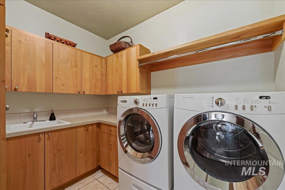 Laundry room featuring cabinet space, washing machine and clothes dryer, light tile patterned floors, and a textured ceiling