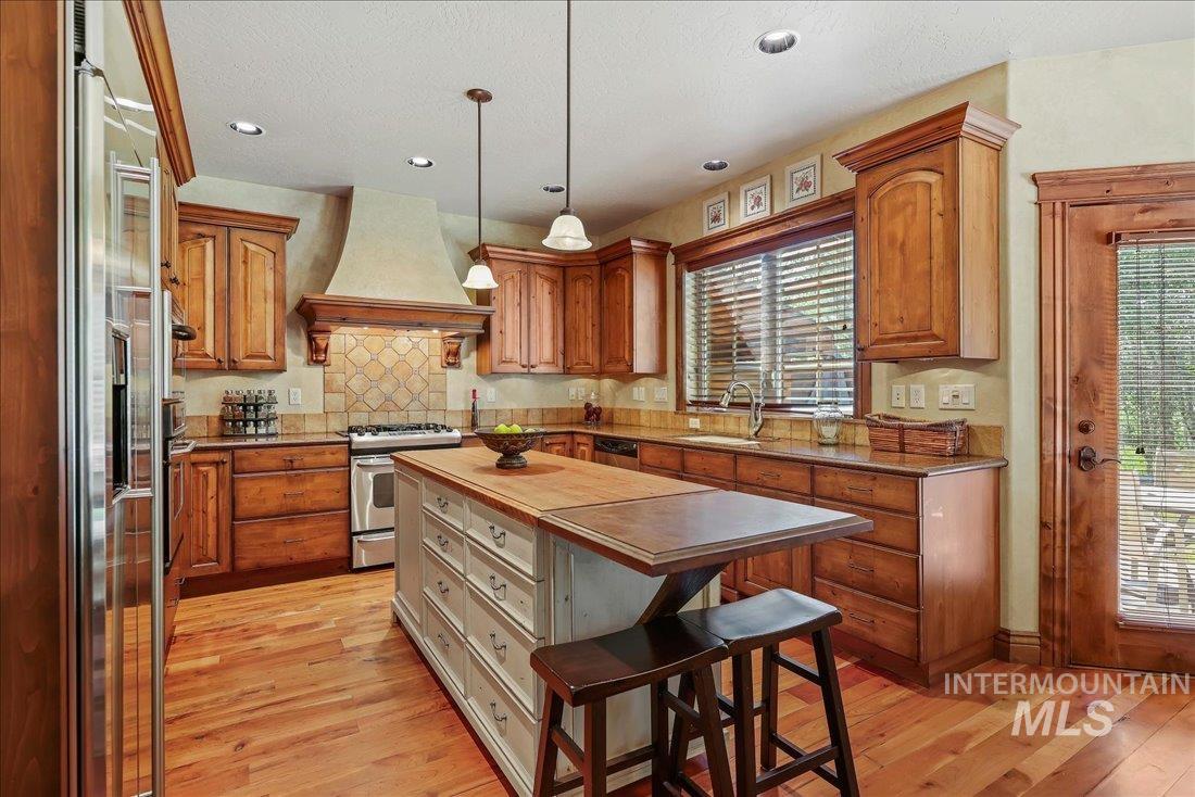 Kitchen featuring stainless steel range with gas cooktop, custom range hood, built in refrigerator, wood-flooring, and butcher block counters