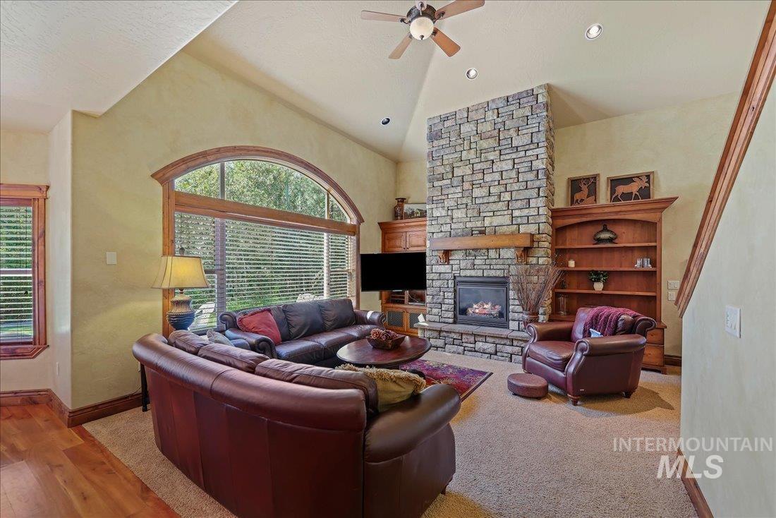 Living room with ceiling fan, plenty of natural light, vaulted ceiling, a fireplace, and wood floors