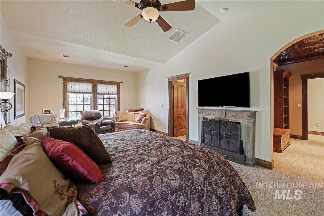 Carpeted bedroom featuring arched walkways, a fireplace, lofted ceiling, and a ceiling fan