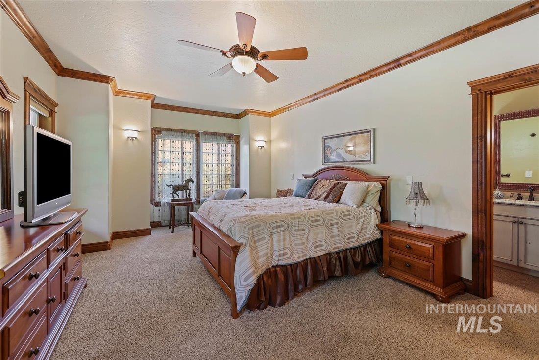 Bedroom with light colored carpet, crown molding, ensuite bathroom, a ceiling fan, and a textured ceiling