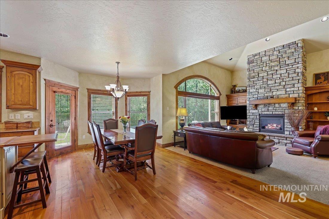 Dining space with a chandelier, wood floors, a textured ceiling, and a stone fireplace
