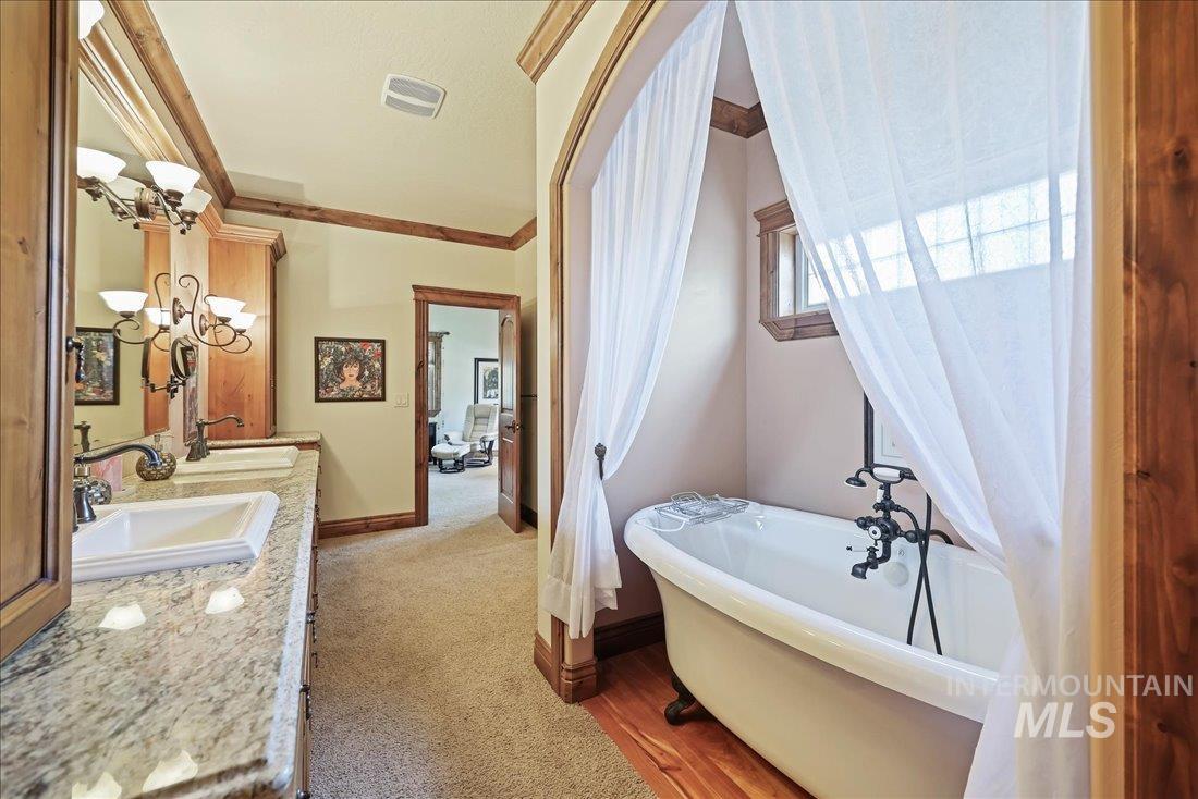 Full bath featuring a chandelier, a soaking tub, double vanity, and ornamental molding