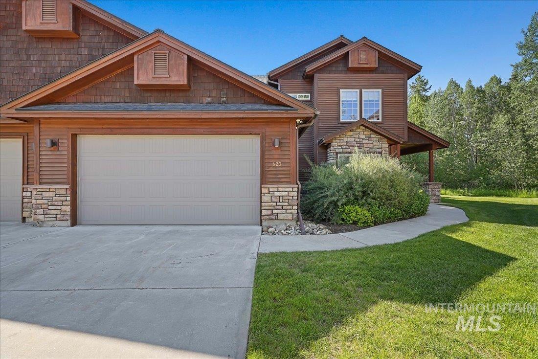 View of front of property featuring stone siding, a front yard, concrete driveway, and an attached garage