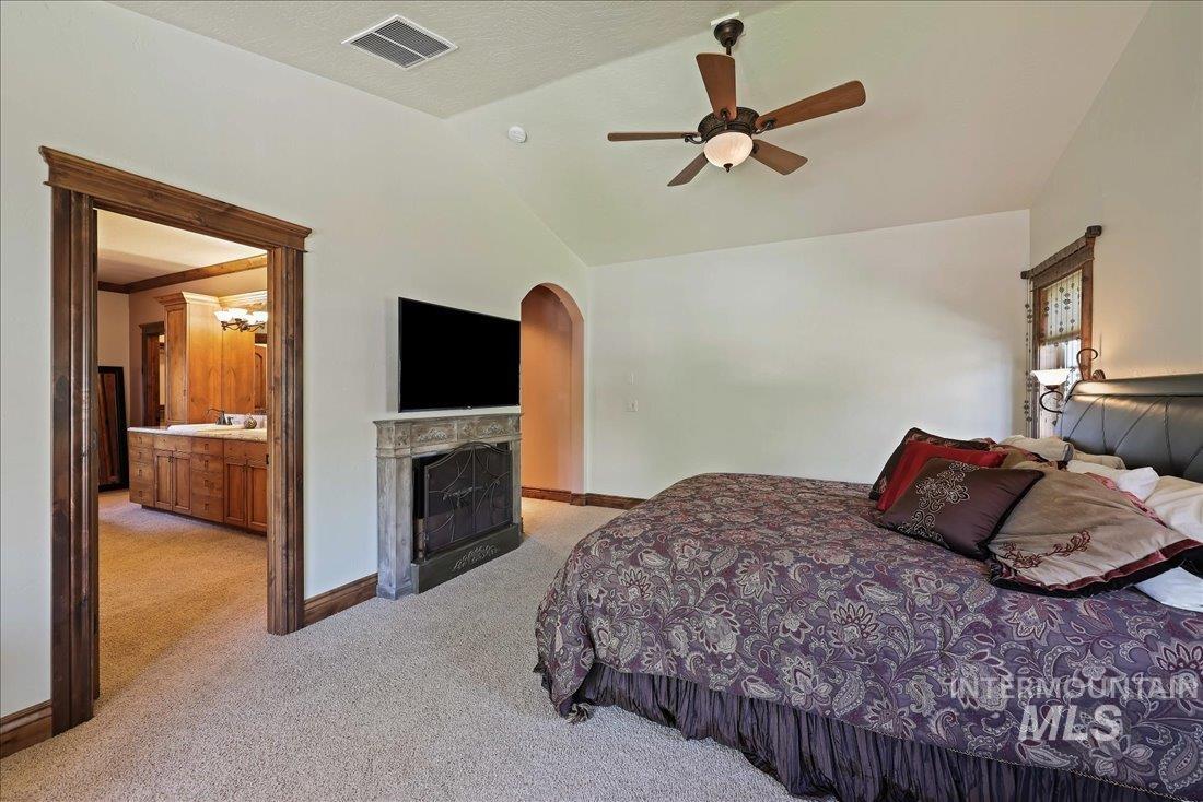 Bedroom featuring light colored carpet, arched walkways, lofted ceiling, a fireplace, and ceiling fan