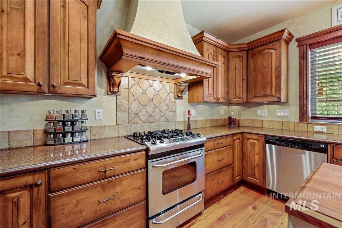 Kitchen with stainless steel appliances, custom range hood, wood floors, and beautiful cabinets
