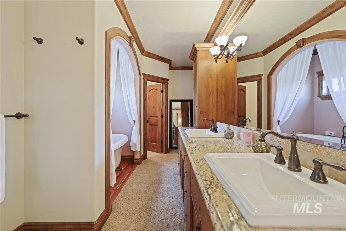 Bathroom featuring double vanity, a soaking tub, a chandelier, and crown molding