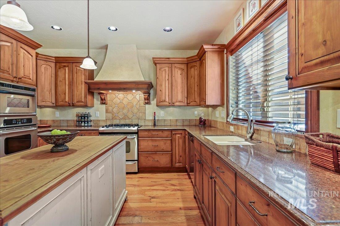 Kitchen featuring stainless steel appliances, custom range hood, butcher block countertops, pendant lighting, and wood floors