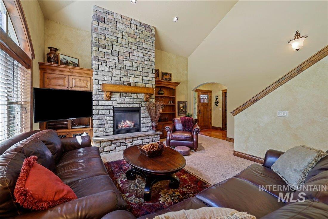 Living room featuring high vaulted ceiling, healthy amount of natural light, a stone fireplace, arched walkways, and carpet flooring