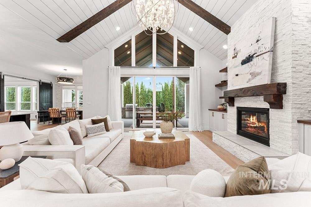 Living area with wood finished floors, a chandelier, high vaulted ceiling, a stone fireplace, and recessed lighting