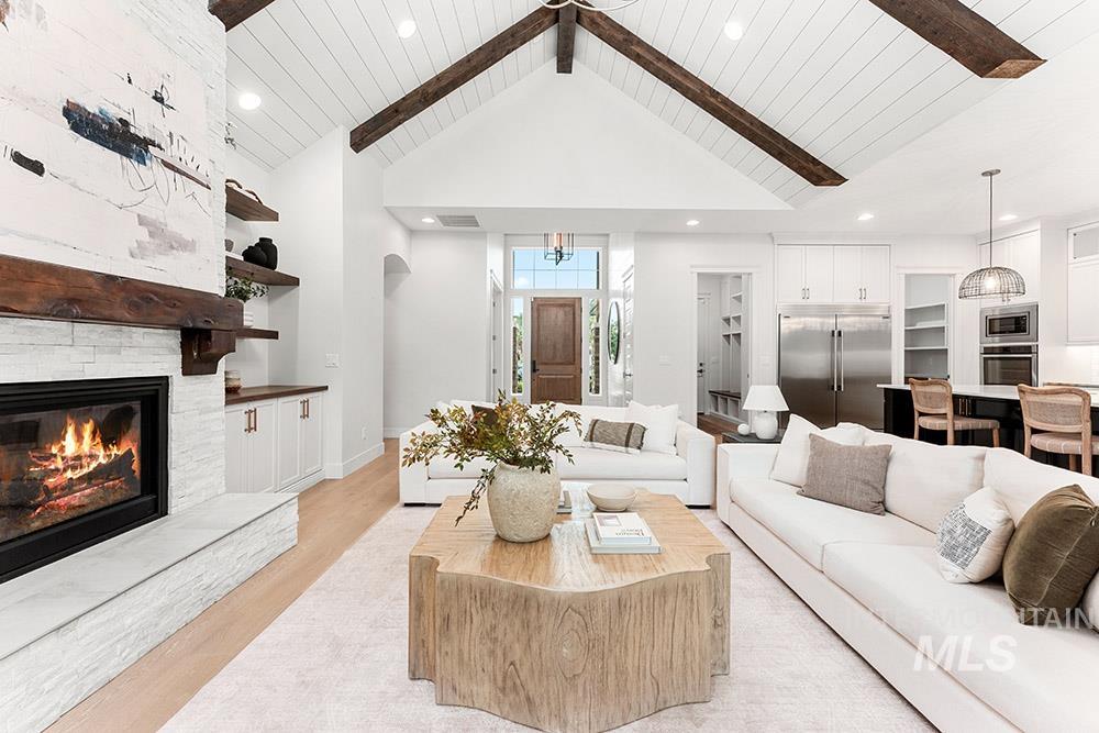 Living room featuring light wood-style flooring, beam ceiling, high vaulted ceiling, recessed lighting, and a stone fireplace
