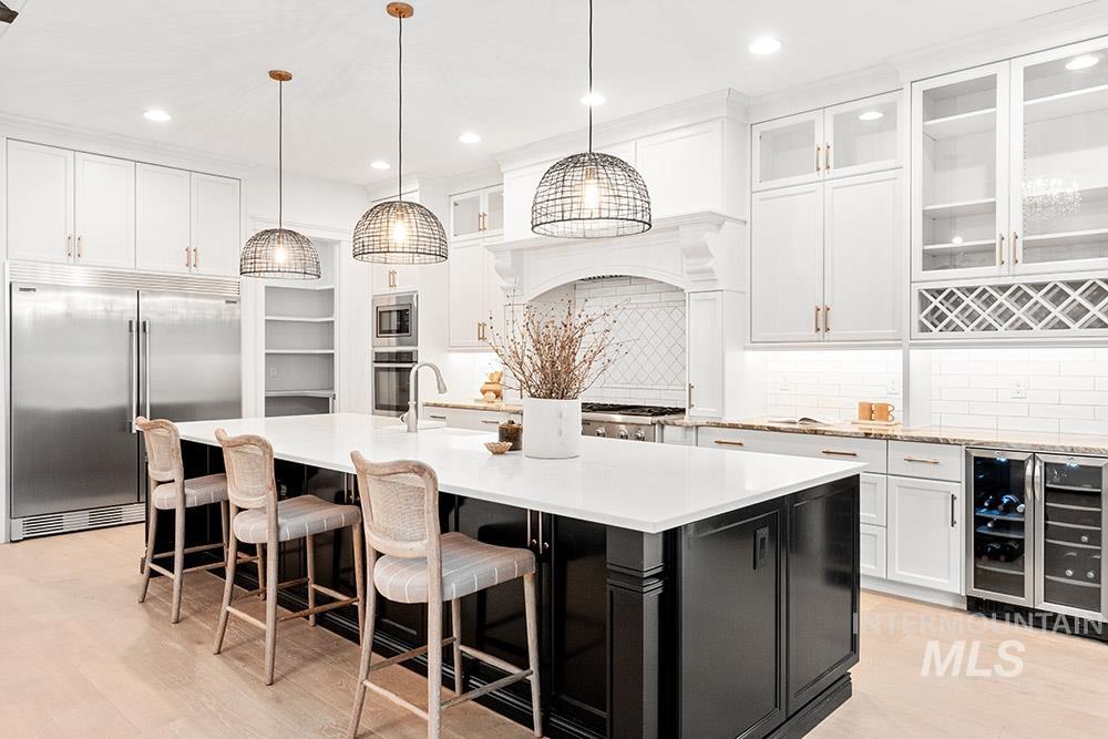 Kitchen with dark cabinetry, beverage cooler, built in appliances, white cabinetry, and decorative backsplash