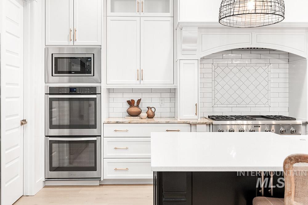 Kitchen featuring white cabinetry, decorative backsplash, appliances with stainless steel finishes, light stone countertops, and glass insert cabinets