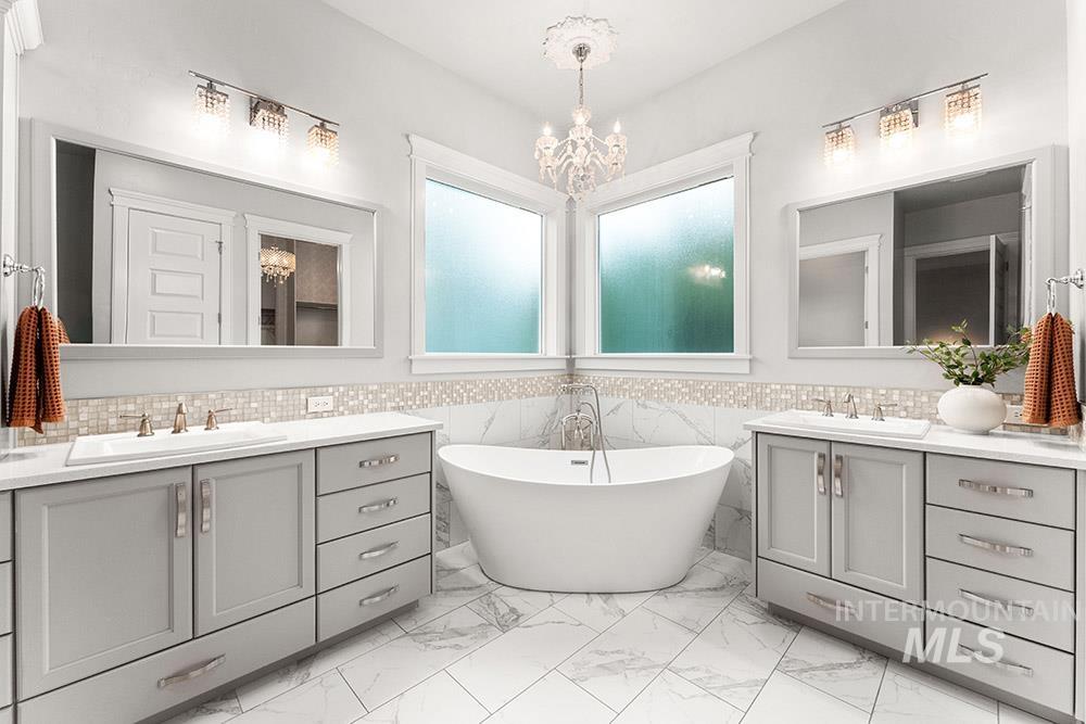 Full bathroom featuring two vanities, a freestanding tub, light marble finish flooring, tile walls, and a chandelier