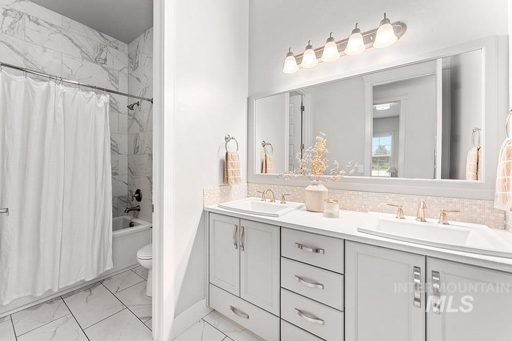Full bath with shower / bath combo, double vanity, tasteful backsplash, and light marble finish flooring