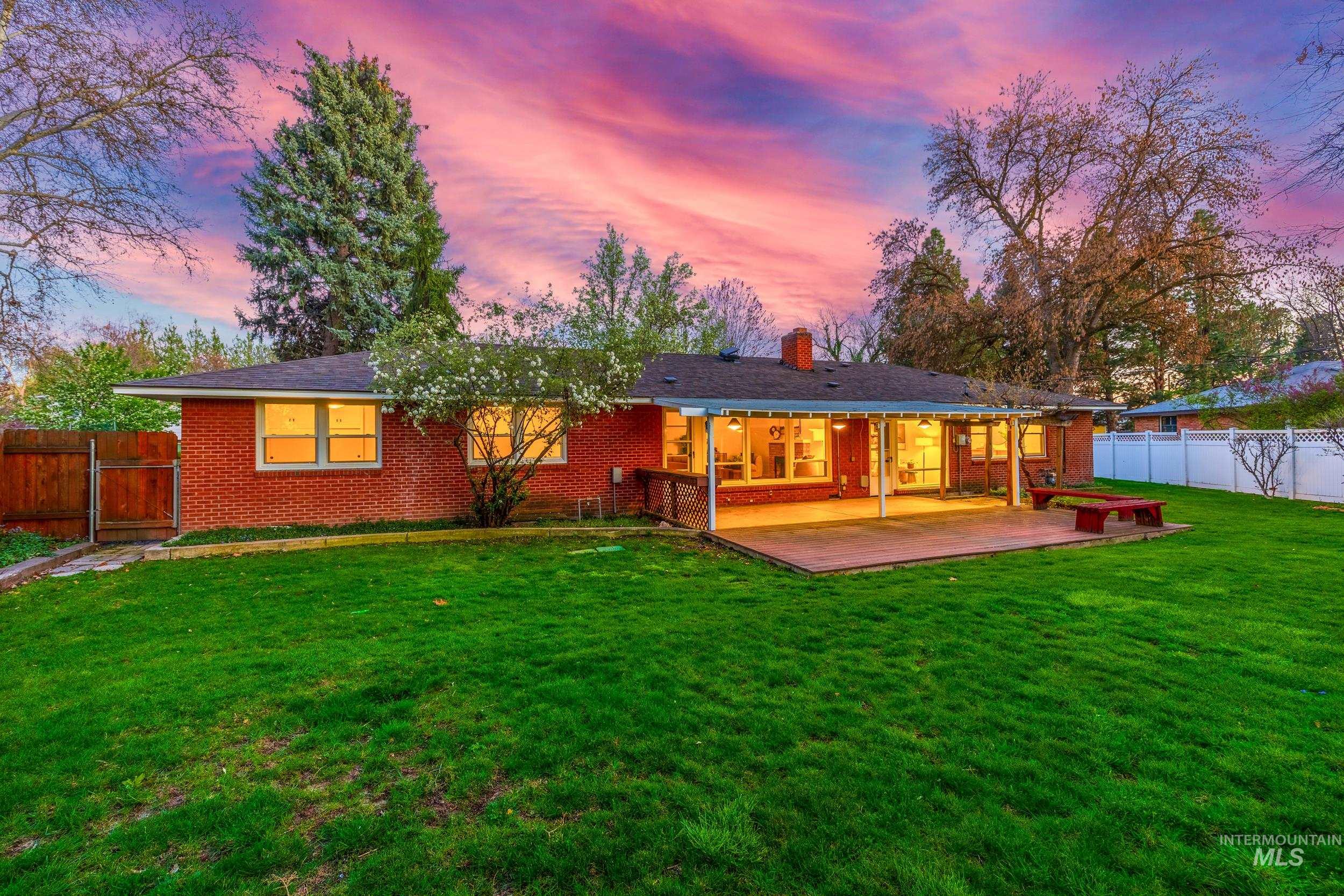 Back of house at dusk featuring a fenced backyard, brick siding, a chimney, a gate, and a patio area