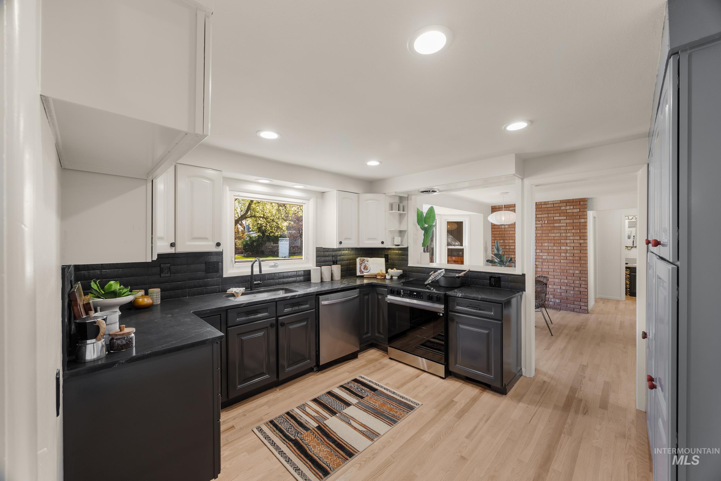 Dual tone kitchen with dual tone cabinetry, black range with electric stovetop, light wood finished floors, stainless steel dishwasher, and decorative backsplash