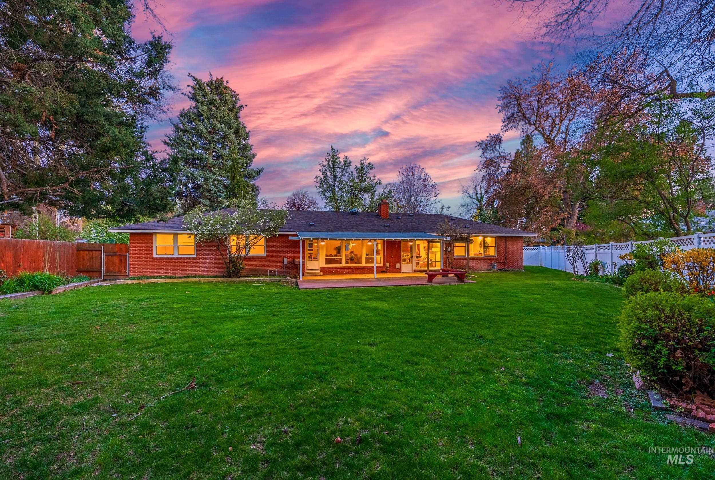 Back of property at dusk featuring a fenced backyard, a patio area, brick siding, and a chimney
