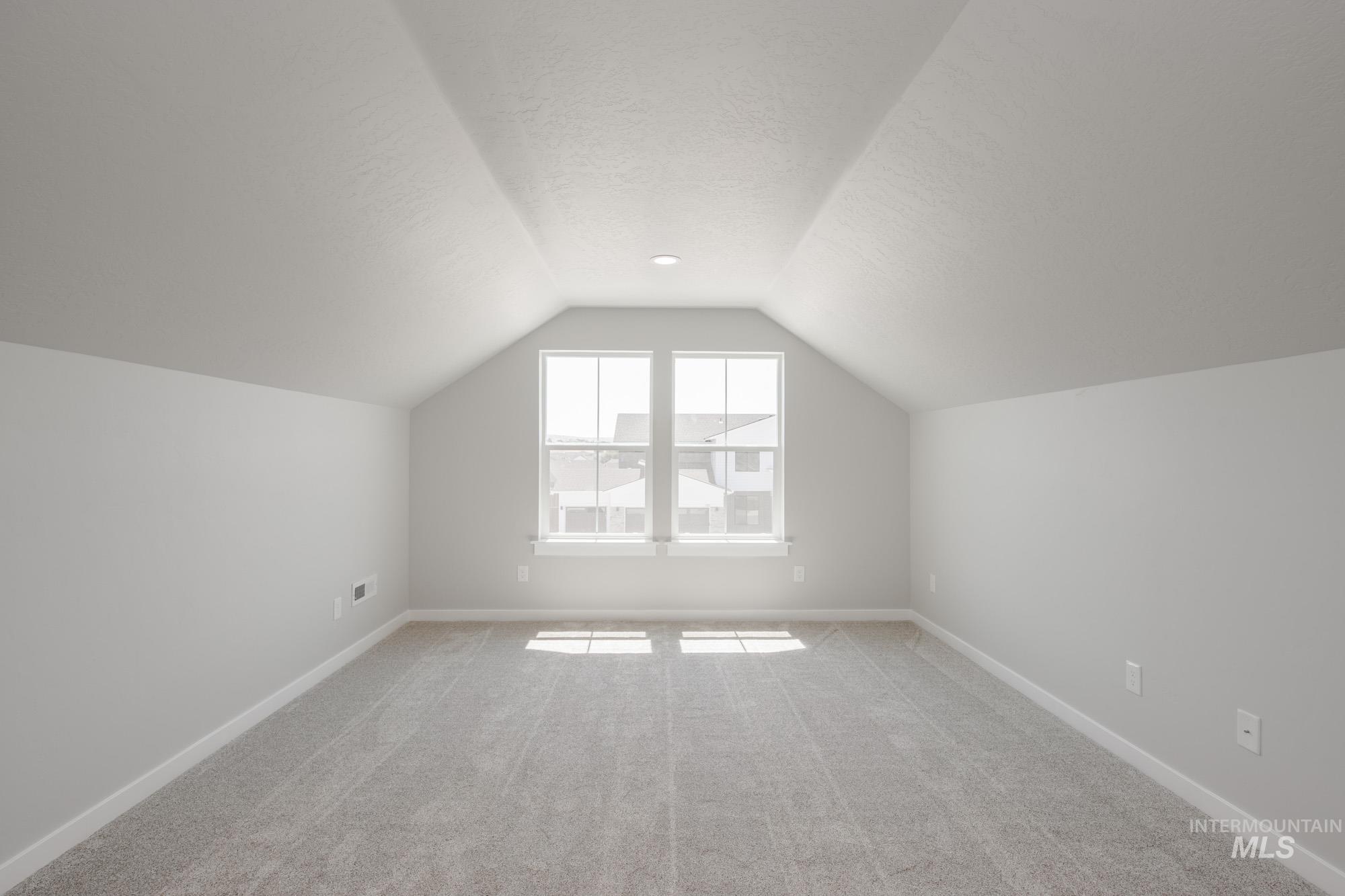 Bonus room with light colored carpet, lofted ceiling, and a textured ceiling