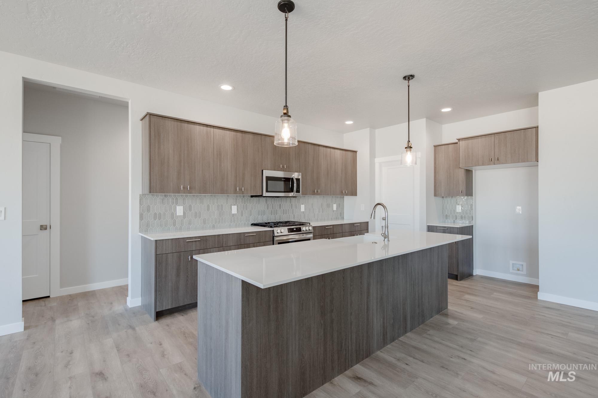 Kitchen featuring decorative backsplash, modern cabinets, light countertops, appliances with stainless steel finishes, and light wood-type flooring