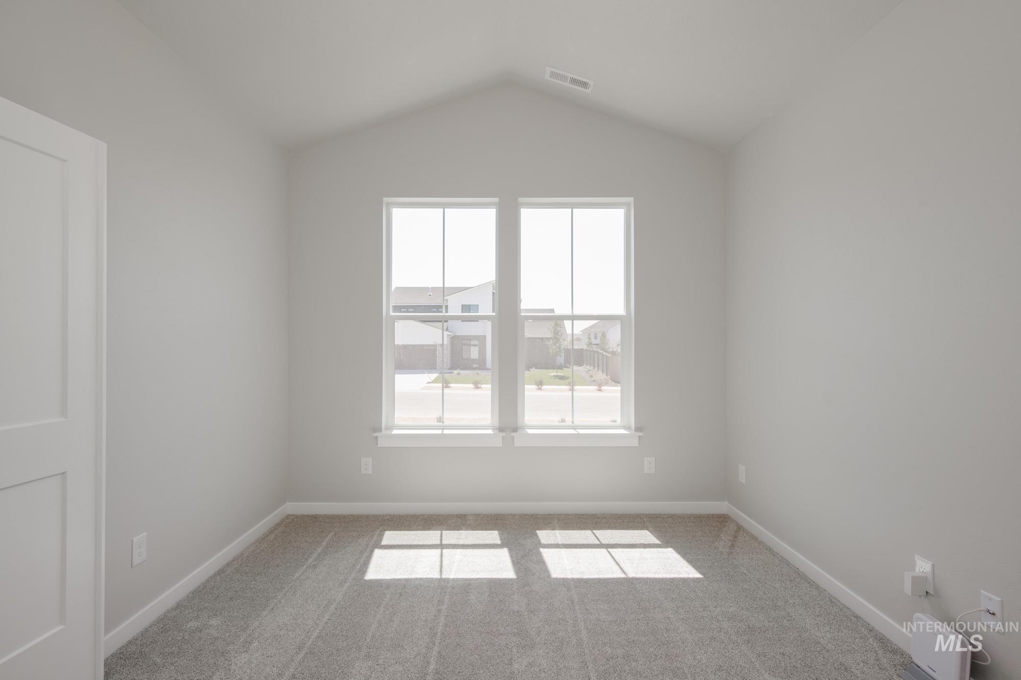 Spare room featuring light colored carpet and vaulted ceiling