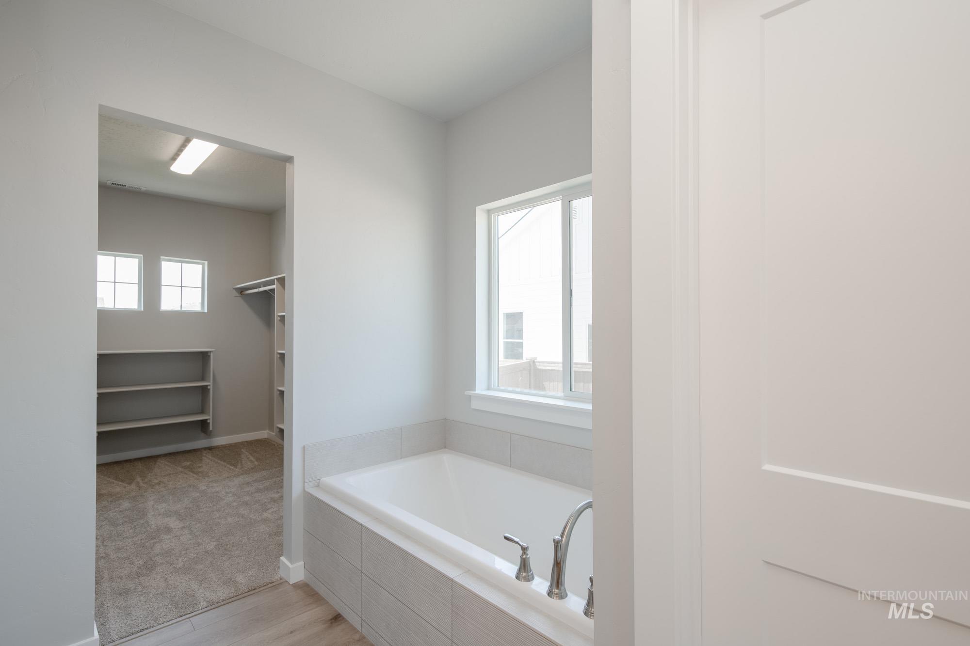 Bathroom with plenty of natural light, a bath, a spacious closet, and wood finished floors