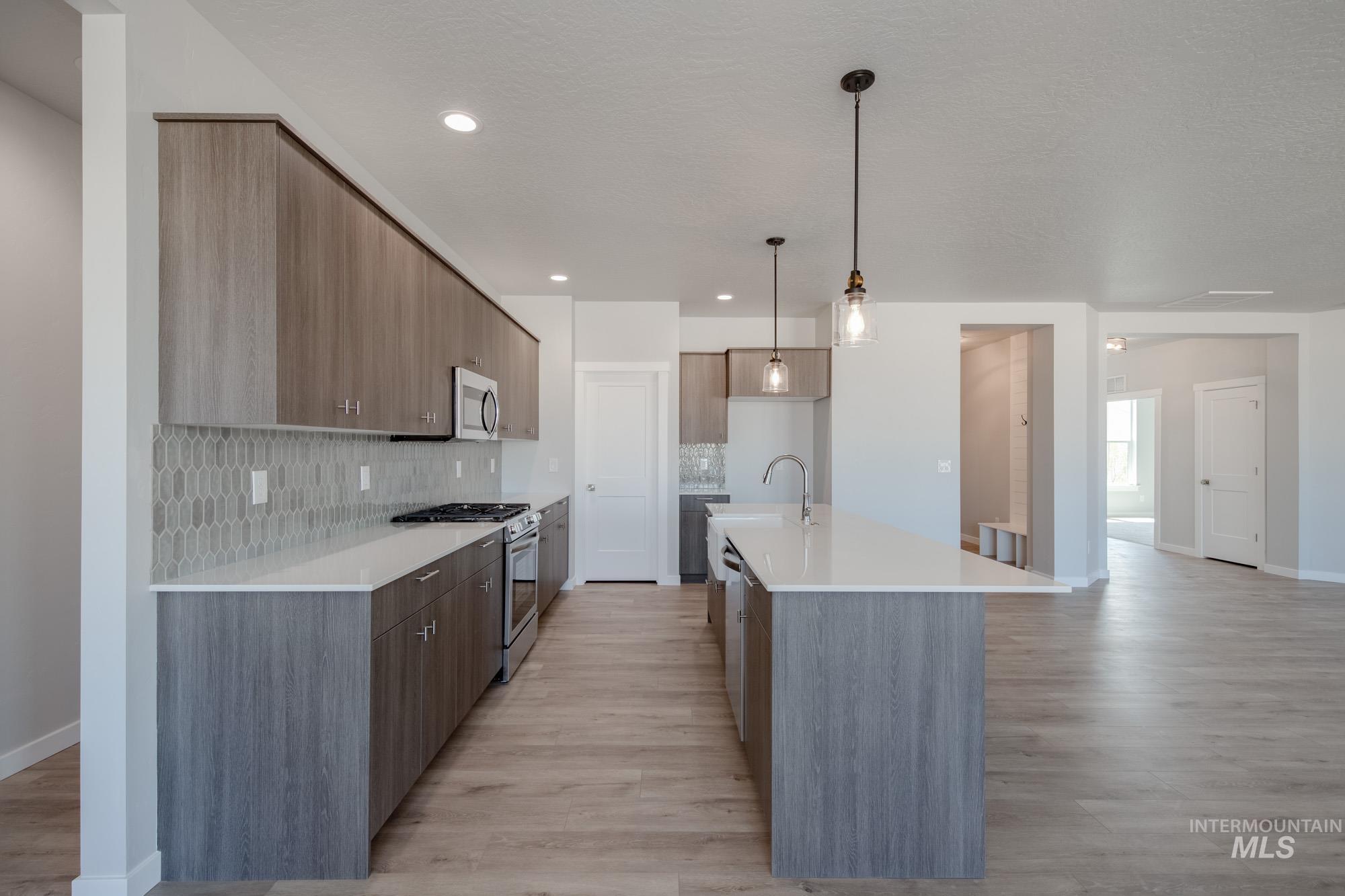 Kitchen featuring stainless steel appliances, backsplash, modern cabinets, light countertops, and light wood-style flooring