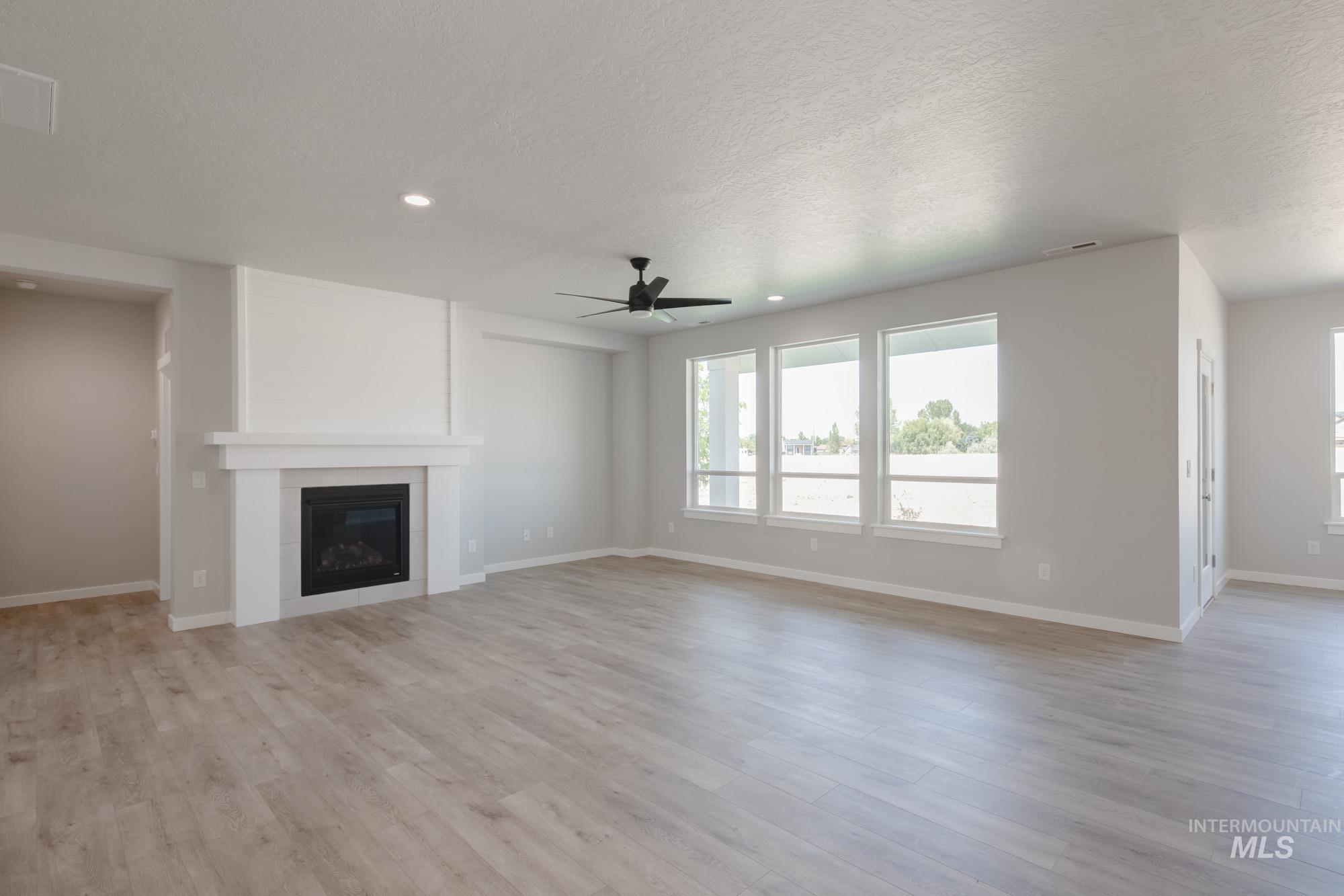 Unfurnished living room featuring a fireplace, light wood-type flooring, ceiling fan, recessed lighting, and a textured ceiling
