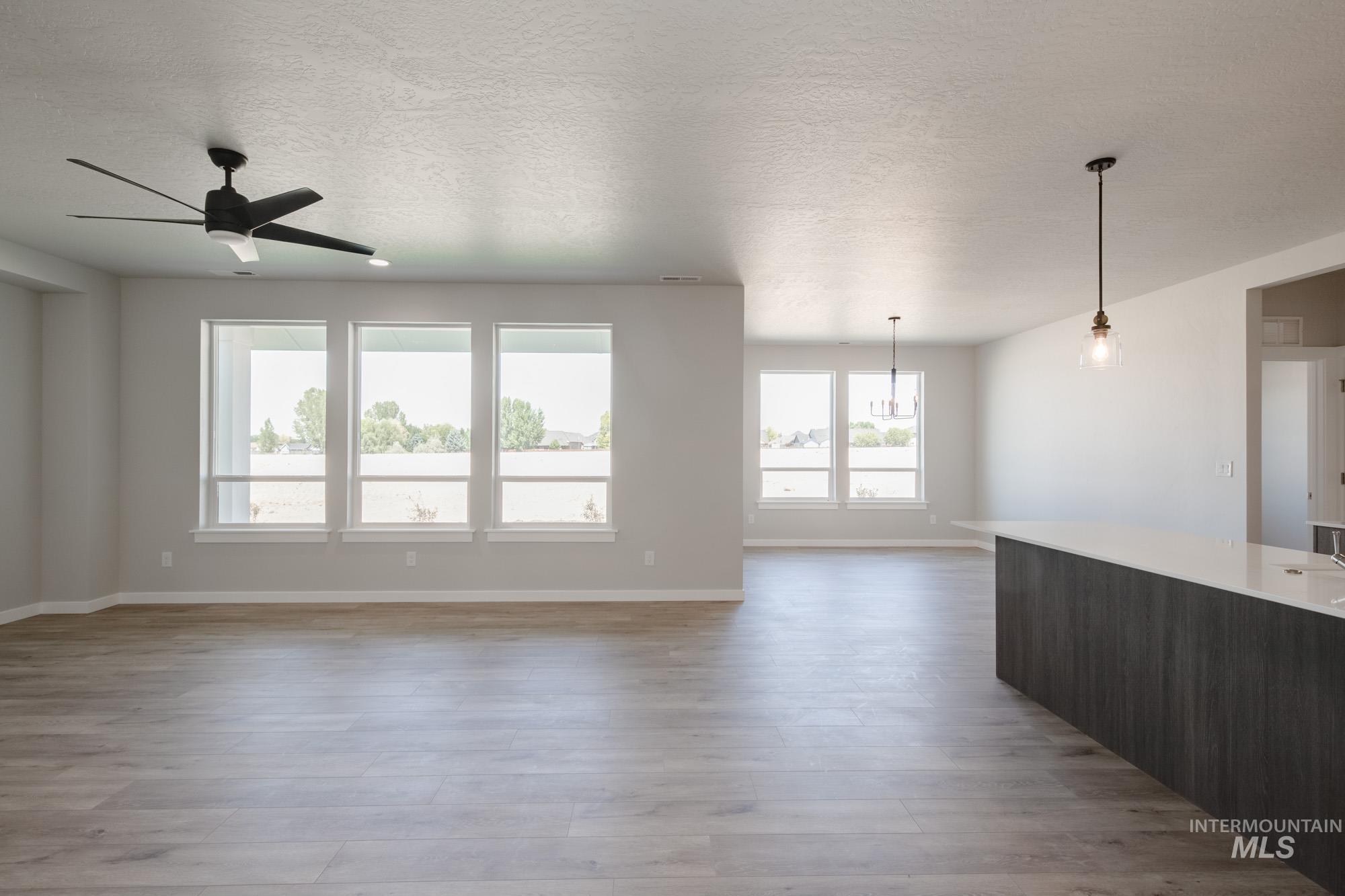 Unfurnished living room with a textured ceiling, light wood-style floors, and a ceiling fan